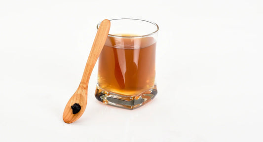 Shilajit in a glass and a wooden spoon on the right