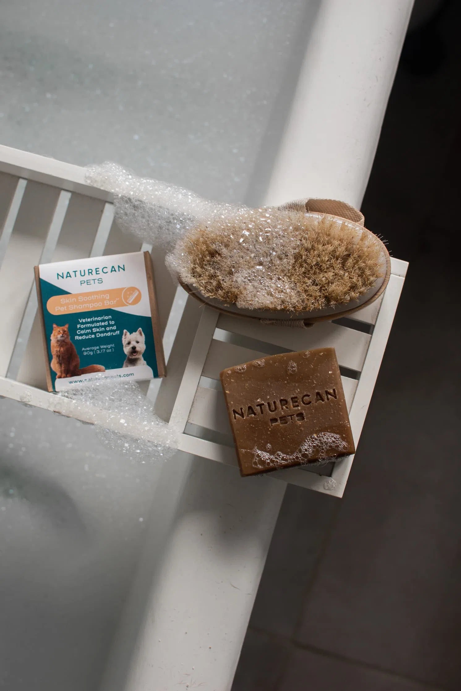 Naturecan pet shampoo bar with brush and bubbles on a bath tray.