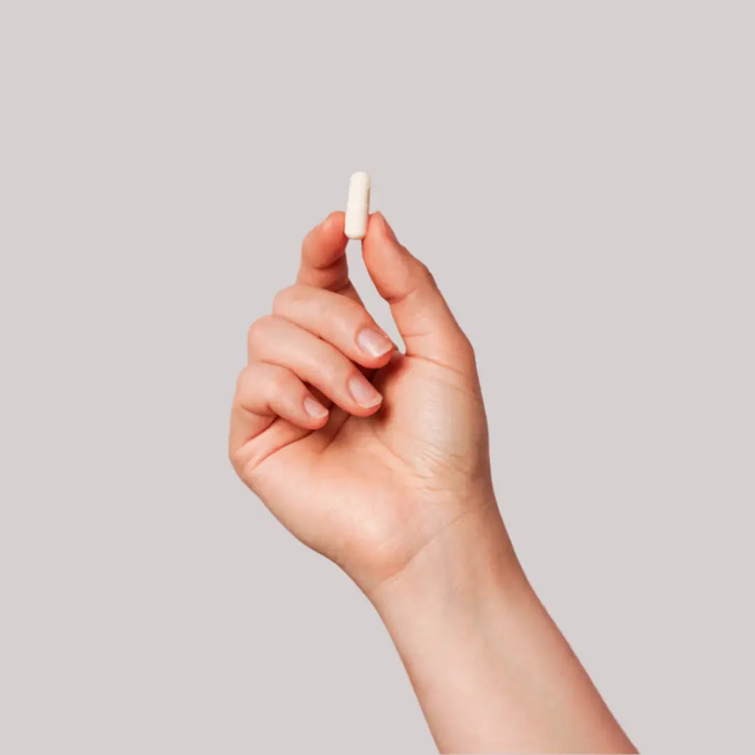 Hand holding a small white capsule against a neutral background.