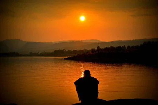 Lonely man sitting by the sea during sunset