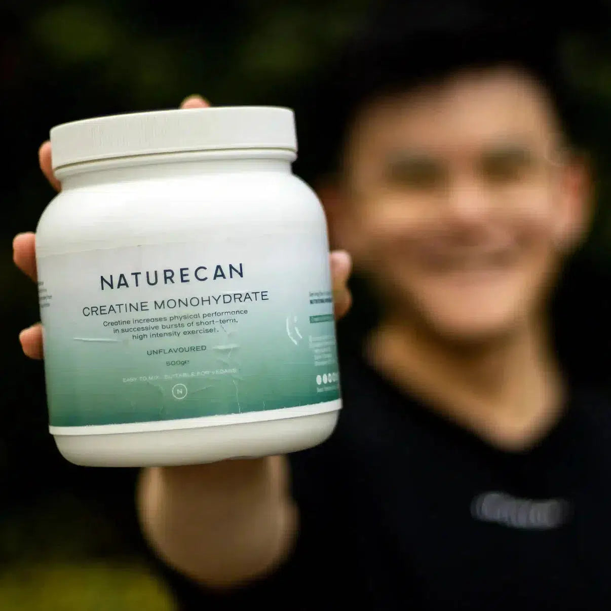 Person holding a Naturecan Creatine Monohydrate container with a smile, focus on the product.