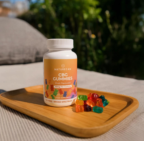 Naturecan CBG Gummies bottle on a tray with colorful gummies spread out beside it.