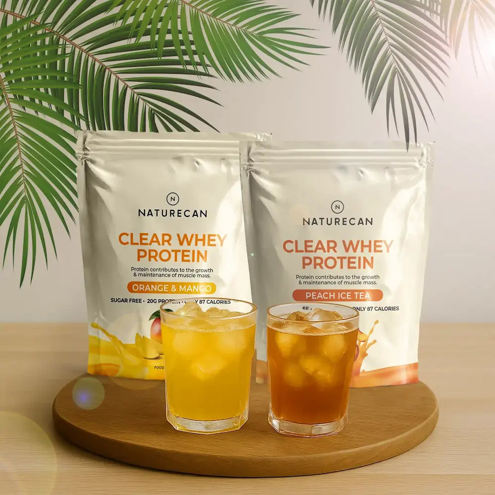 Naturecan Clear Whey Protein packages with two glasses of flavored tea on a wooden board against a leafy green background.