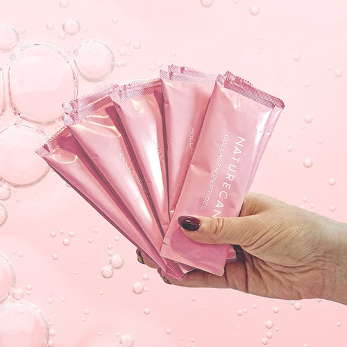Hand holding pink Naturecan collagen peptide sticks with a bubble background.