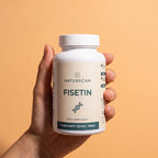 A hand holding a white bottle of Naturecan Fisetin food supplement against a solid peach-colored background.