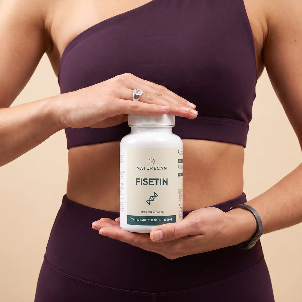 A woman in a dark purple sports bra and leggings holds a white bottle of Naturecan Fisetin dietary supplement against a solid beige background.