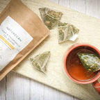 Naturecan hemp and chamomile tea blend with tea bags and brewed tea in a red mug on a wooden surface.