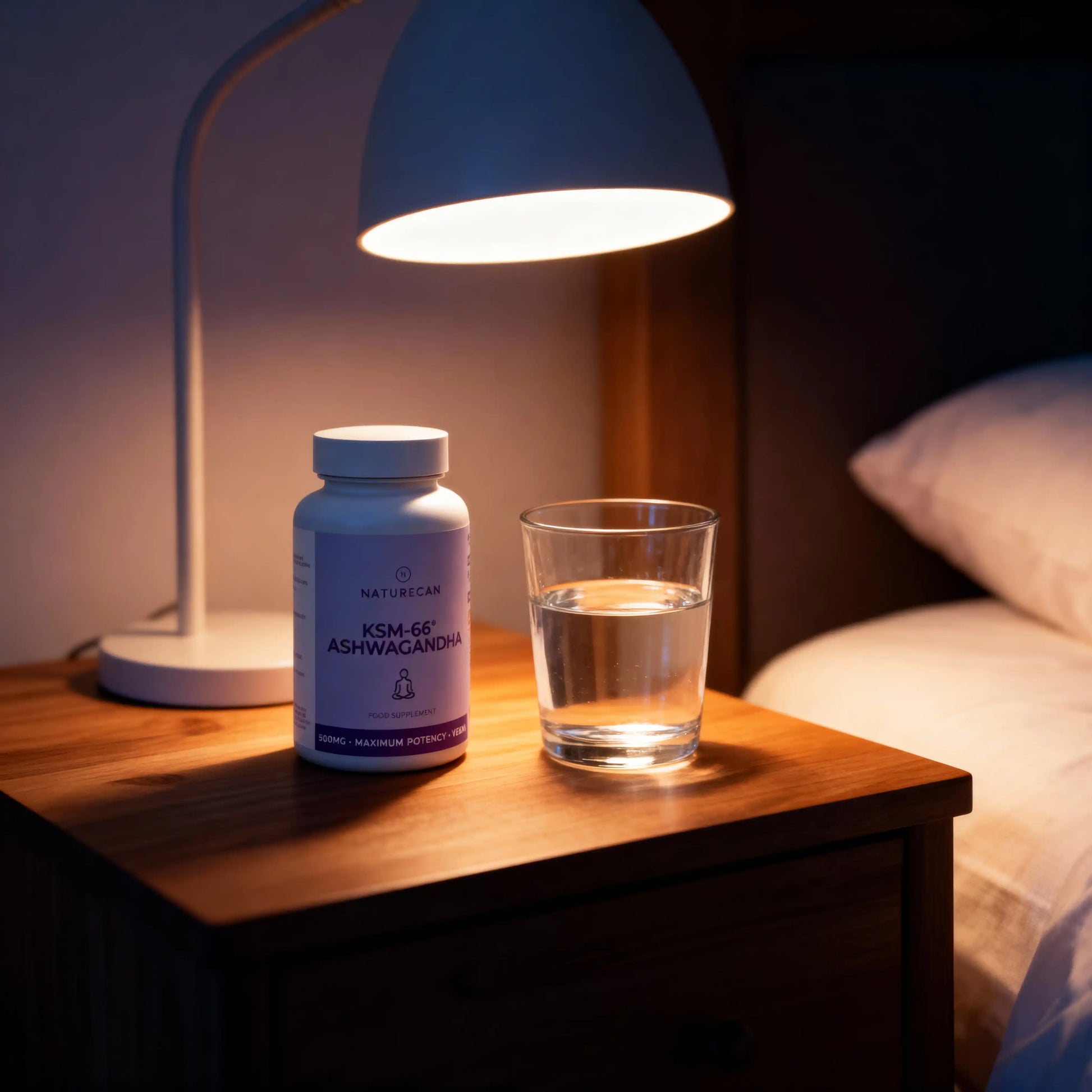 KSM-66 Ashwagandha supplement bottle and glass of water on a nightstand under a lamp.