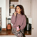 Woman sitting at a kitchen counter with a pink jar, surrounded by kitchen appliances and decor.