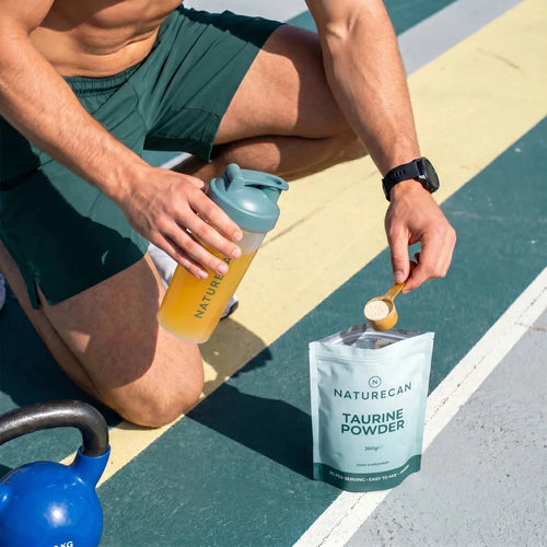 Person holding a bottle and a packet of Naturecan Taurine Powder on a colorful outdoor floor.