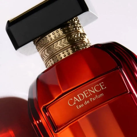 Cadence Eau de Parfum bottle in a glossy translucent red glass, featuring a textured gold neck collar and a black rectangular cap, shown on a clean white background.
