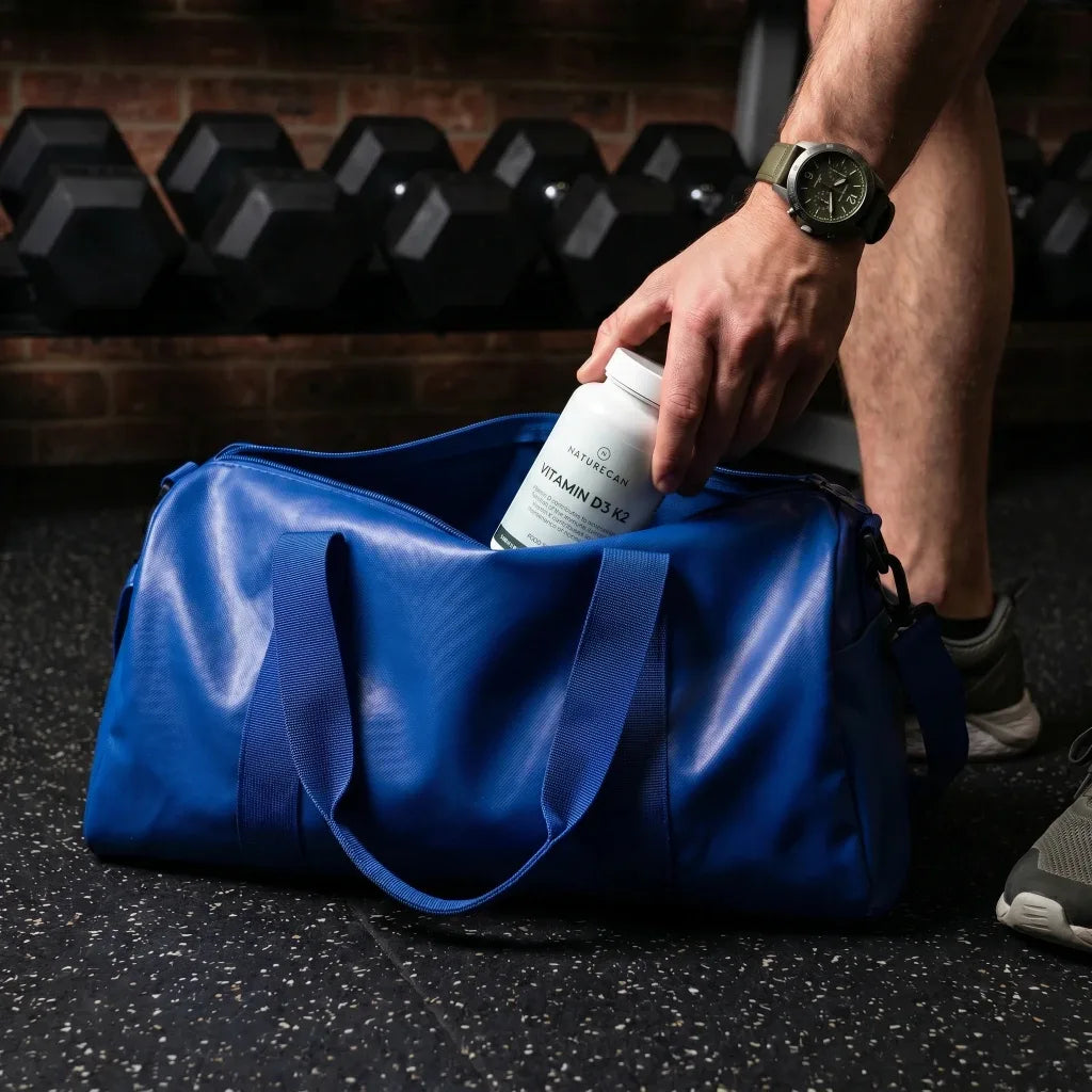 Person placing a supplement container into a blue gym bag in a gym setting